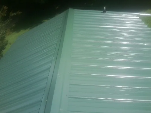 New green metal panels meeting at the ridge of a roof — Flat Roof Repair work by our crew in Norton