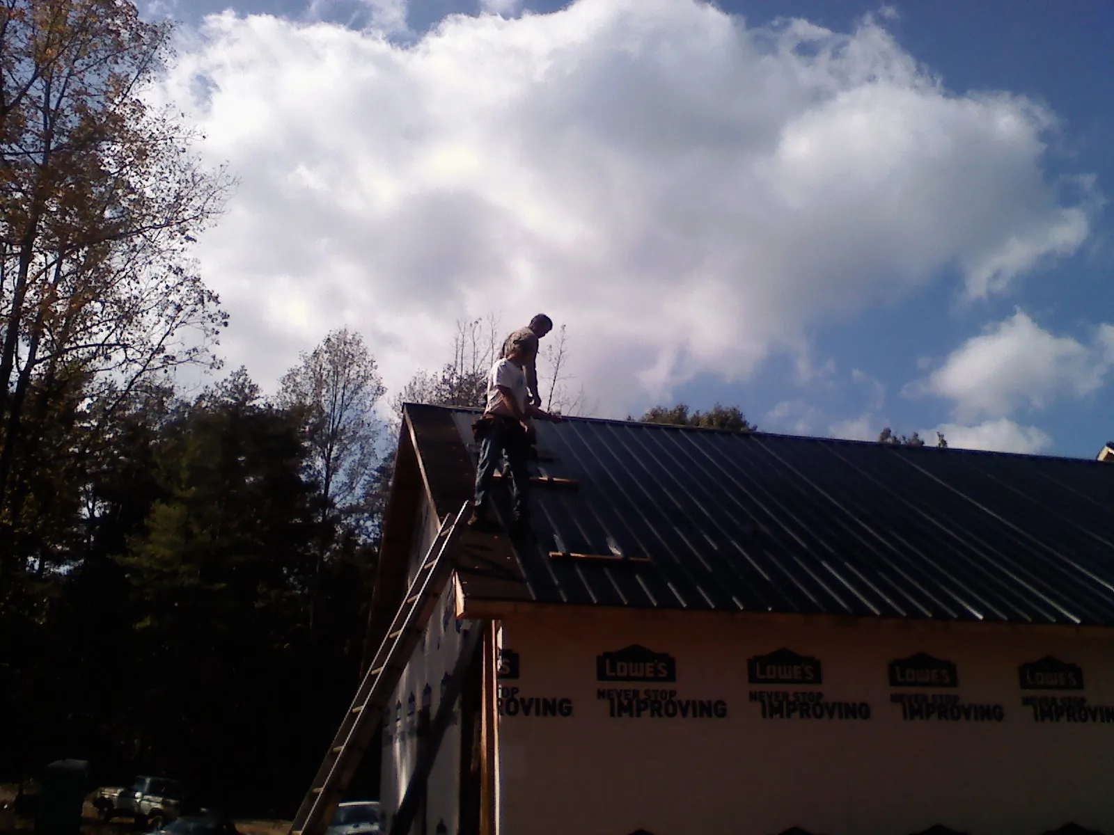 Roofer fastening dark metal panels high against a cloudy sky, from a Roof Inspection job in Norton