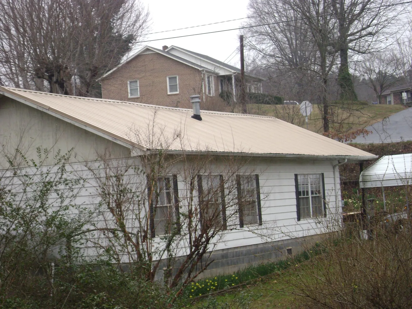 Tan metal roof on a white sided house set into a hillside — Commercial Roofing by Roofing Brothers in Norton