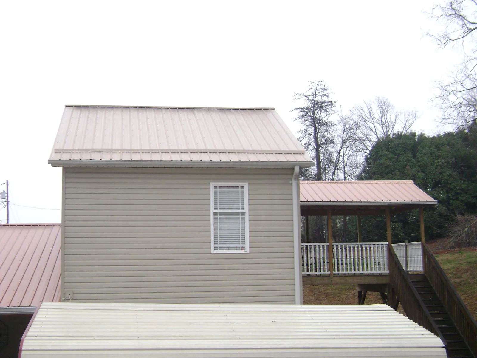 Tan metal roofs on a two story addition and attached porch, from a Roof Replacement job in Norton